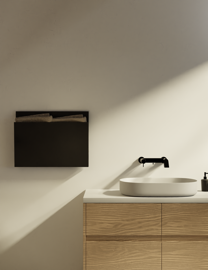 MG12 Geometrici Magazine towel warmer in black above a wood vanity with a vessel sink