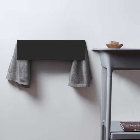 MG12 MiniSlim electric towel warmer in matte black, wall-mounted with grey towels in a minimalist bathroom